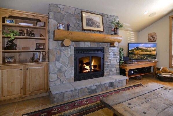 Una chimenea de piedra con fuego de leña, un mueble de madera para entretenimiento y un televisor.