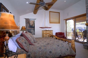 Un dormitorio con una cama, un ventilador de techo, un aparador de madera, una silla roja y un ventanal grande.