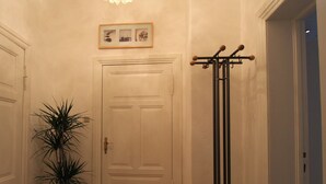 Un pasillo con piso de madera, una puerta blanca, una planta en maceta, un perchero y un cuadro sobre la puerta.