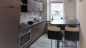 Cocina compacta con estufa, horno y pileta, una pequeña mesa de comedor con dos sillas, y un ventanal que proporciona luz natural.