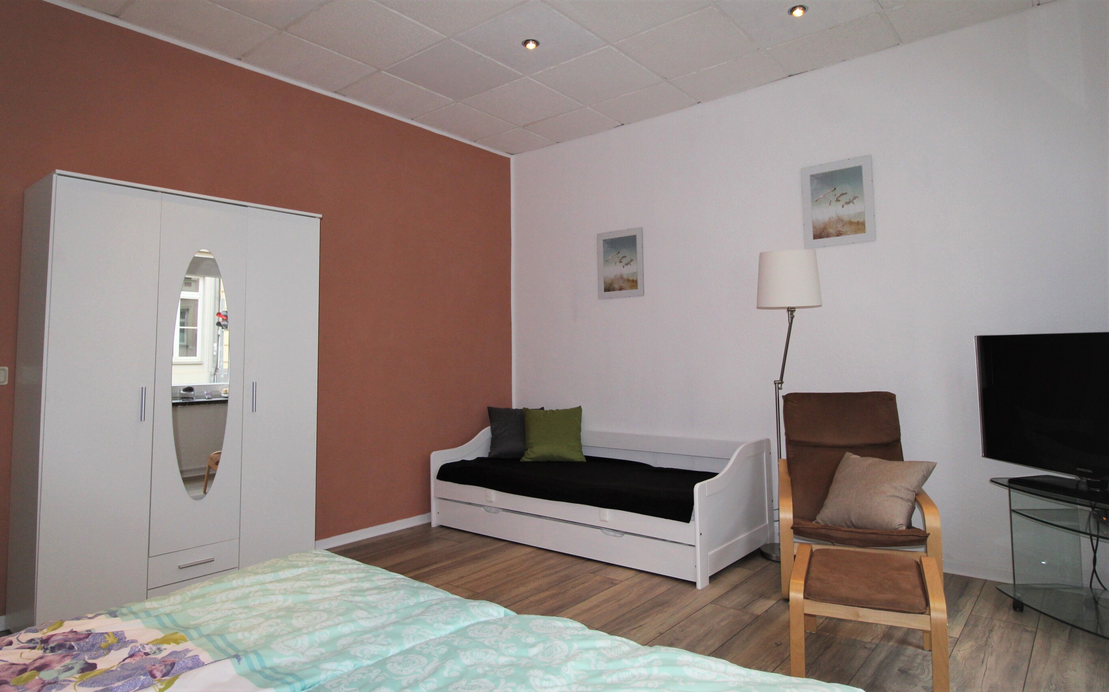 A bedroom with a bed, a wardrobe, a chair, a desk, and a TV.