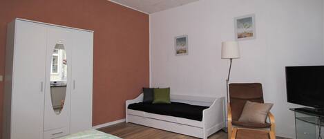 A bedroom with a bed, a wardrobe, a chair, a desk, and a TV.