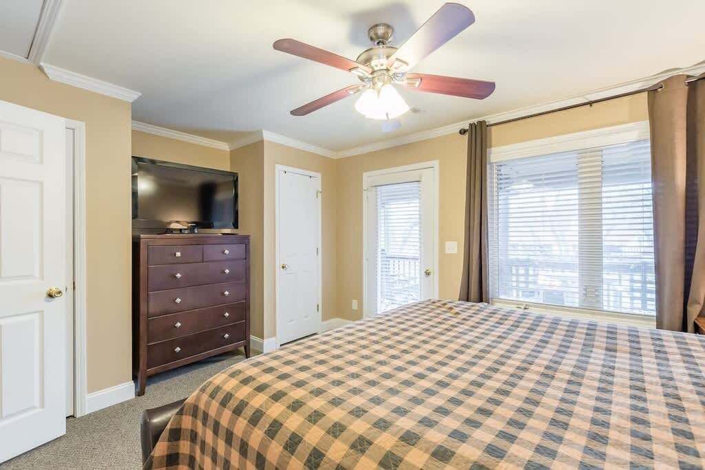 Ein Schlafzimmer mit Bett, Schminktisch, Deckenventilator und einem Fenster mit Jalousien.