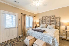 A bedroom with a bed, a ceiling fan, a door, and a window with curtains.