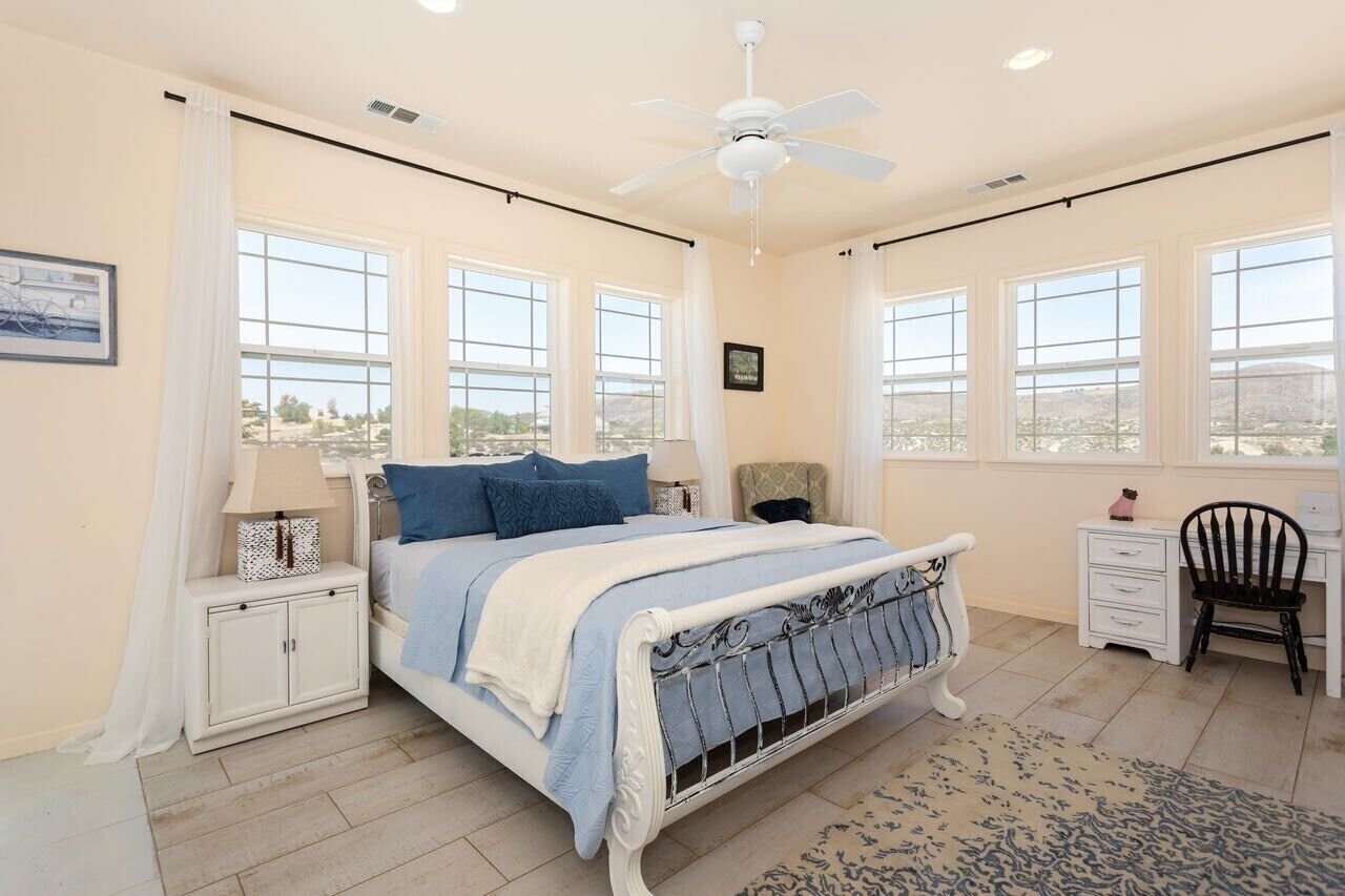 A bedroom with a bed, a nightstand, a chair, a desk, and a window with a view.