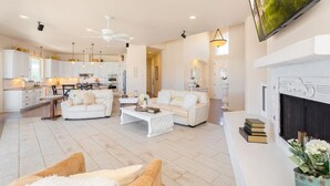 A spacious living area with a fireplace, white furniture, and a kitchen in the background. - Breathtaking view with a heated lap pool and pick ball court  (Temecula)