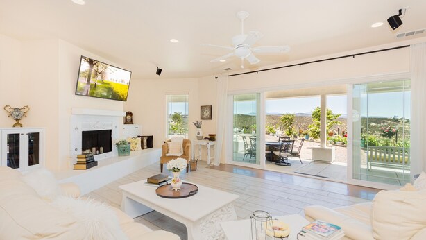 A spacious living room with a fireplace, comfortable seating, and a large sliding glass door leading to an outdoor patio. - Breathtaking view with a heated lap pool and pick ball court  (Temecula)