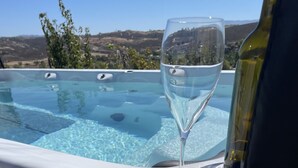 A glass of white wine on a poolside table with a bottle of wine, overlooking a pool with a scenic view of hills and trees. - Breathtaking view with a heated lap pool and pick ball court  (Temecula)