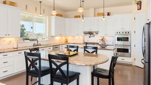 A modern kitchen with white cabinets, a central island with chairs, pendant lighting, and stainless steel appliances. - Breathtaking view with a heated lap pool and pick ball court  (Temecula)