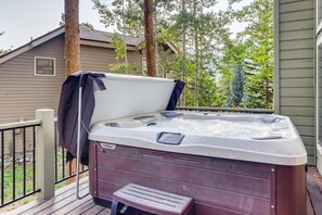 Ett bubbelbad på ett trädäck med en bänk, omgivet av träd och ett hus i bakgrunden.