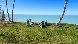 A grassy area with several Adirondack chairs facing a clear blue sky and a calm sea.