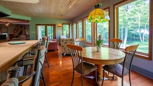 A spacious kitchen with a wooden ceiling, large windows, and a dining area with a round table and chairs.