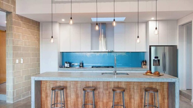 A modern kitchen with a central island, bar stools, a stainless steel refrigerator, and pendant lighting.