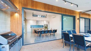 A modern kitchen with a built-in stove, a dining area with a table and chairs, and a large sliding glass door leading to an adjacent room.