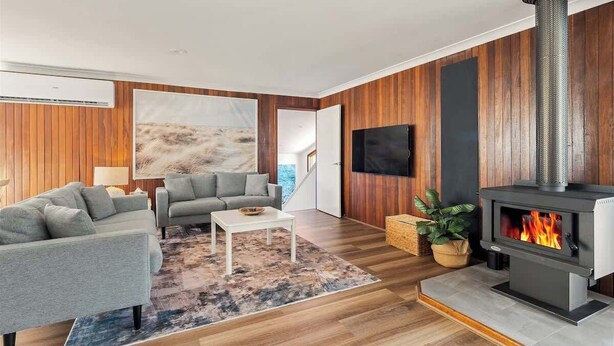 Een moderne woonkamer met een bank, salontafel, open haard en een aan de muur bevestigde televisie.