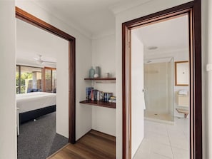 Een slaapkamer met een bed, een klein plankje met boeken, en een badkamer met een douche.