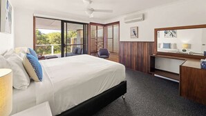 Een hotelkamer met een bed, bureau, stoel, groot raam en plafondventilator.