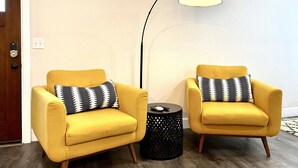 Deux fauteuils jaunes ornés de coussins à motifs, un lampadaire noir et une petite table d’appoint noire avec une télécommande.