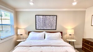 Un lit bien fait, avec du linge de lit blanc, deux lampes de chevet, un élément décoratif mural et une commode en bois.