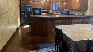 Una cocina con armarios de madera, un refrigerador de acero inoxidable, un horno empotrado y un comedor con mesa y sillas.