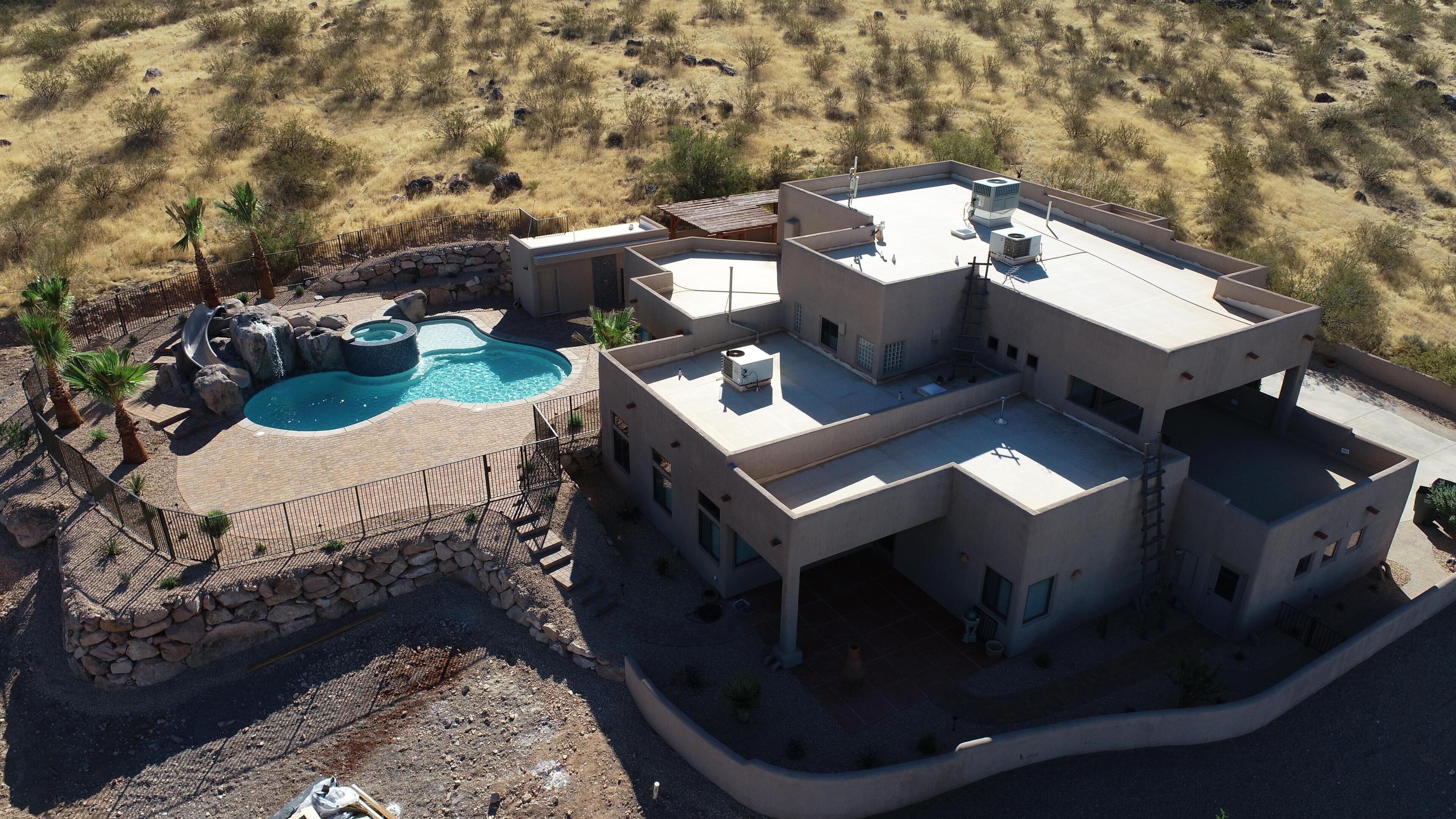 Une maison moderne à plusieurs étages, dotée d’une piscine, et entourée d’un paysage désertique.