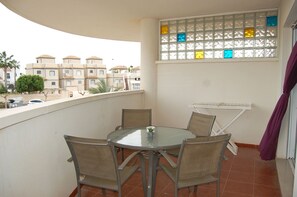 Uma varanda com uma mesa redonda e quatro cadeiras, uma janela com vitrais coloridos e vista para edifícios vizinhos.