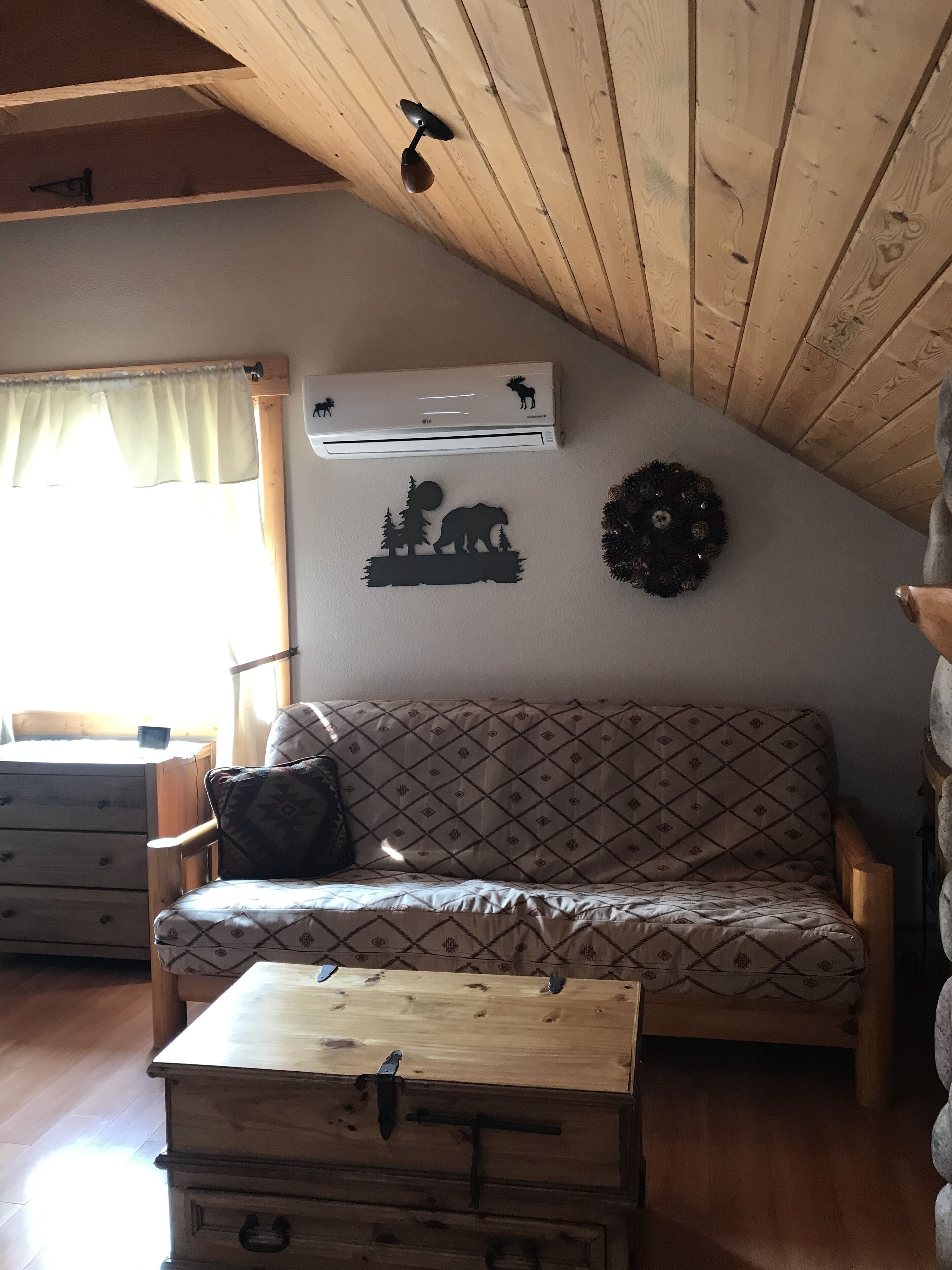 A cozy room with a wooden ceiling, a sofa, a chest of drawers, and a wall-mounted air conditioner.