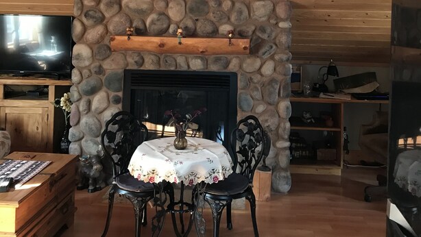 A cozy living room with a stone fireplace, wooden ceiling beams, a television, and a dining table with chairs. - Moose Lodge Loft at Rigden Farms (Fort Collins)