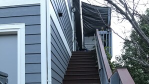 A wooden staircase leading up to a house with grey siding and a metal railing. - Moose Lodge Loft at Rigden Farms (Fort Collins)