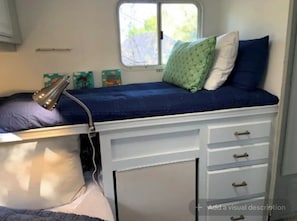 A small, compact room with a bed, a desk, and a window.