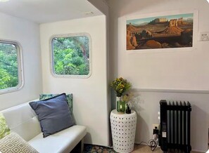 A room with a white sofa, a small table with a vase, a radiator, and a painting on the wall.