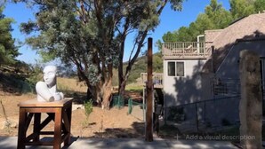 A sculpture of a human figure on a wooden stool, a tree, and a building with a balcony. - Cozy Mallard RV. Light, bright and inspiring trailer amongst the Pine trees. (Topanga)
