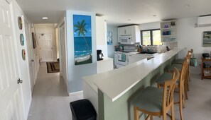 A modern kitchen with a long island, bar stools, and a view of the ocean through the window.