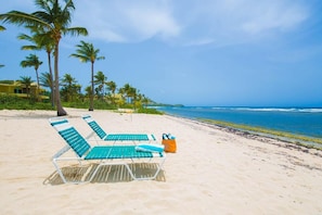 A beach with two green and white lounge chairs, a small orange bag, and a clear view of the ocean.