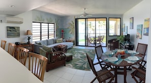 A spacious living area with a sofa, dining table, and chairs, a ceiling fan, and a large sliding glass door leading to an outdoor patio.