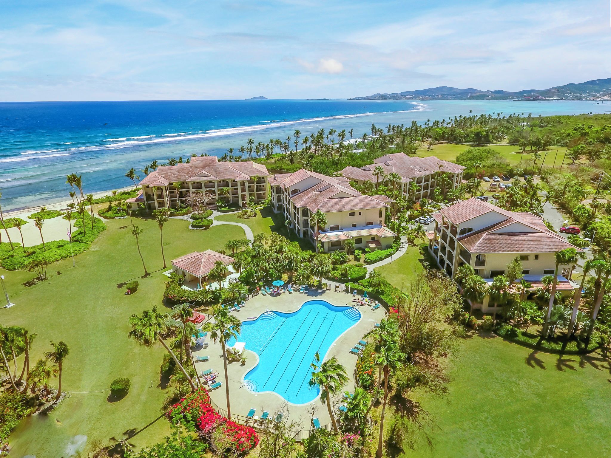 A resort with multiple buildings, a swimming pool, and a beach view.