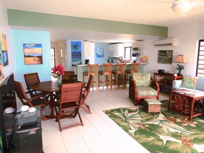 A spacious living area with a dining table, chairs, a sofa, and a kitchen in the background.