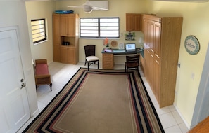 A compact kitchen with wooden cabinets, a dining area with chairs, a laptop on the desk, and a 'Welcome' sign on the wall.