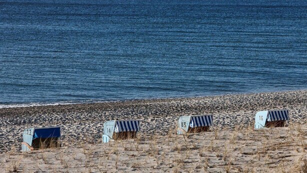 Ein Strand mit mehreren bunten Strandkörben und freiem Blick auf das Meer.