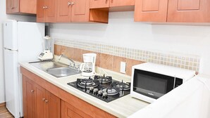 A compact kitchen with wooden cabinets, a gas stove, a coffee maker, and a microwave. - Hospedaje Casa de la Campana Rotamundos (Guanajuato)