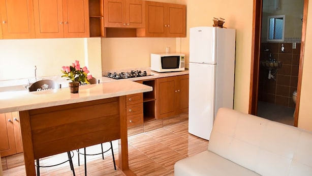 A compact kitchen with wooden cabinets, a white refrigerator, a microwave, and a sink. - Hospedaje Casa de la Campana Rotamundos (Guanajuato)