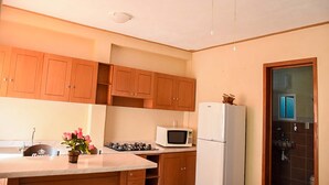 A kitchen with wooden cabinets, a white refrigerator, a microwave, a gas stove, and a ceiling fan. - Hospedaje Casa de la Campana Rotamundos (Guanajuato)