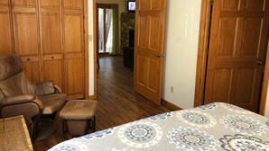 A bedroom with a large bed, a wooden wardrobe, a leather chair, and a television in the background. - Riverfront Condo #1w/patio,1blk 2 town,King bed,ground floor, 40min 2 WinterPark (GRAND LAKE)