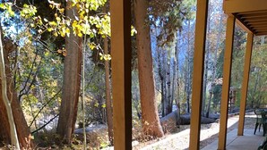 An outdoor patio with a round metal table and black metal chairs, surrounded by trees and a covered walkway. - Riverfront Condo #1w/patio,1blk 2 town,King bed,ground floor, 40min 2 WinterPark (GRAND LAKE)