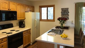 A kitchen with wooden cabinets, a refrigerator, a microwave, a stove, and a window. There is a sign with various phrases on the wall. - Riverfront Condo #1w/patio,1blk 2 town,King bed,ground floor, 40min 2 WinterPark (GRAND LAKE)