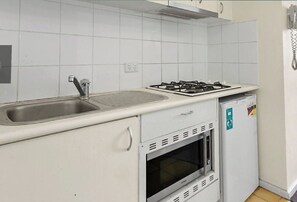 Compact kitchen area with an oven, stainless steel sink, and small refrigerator.