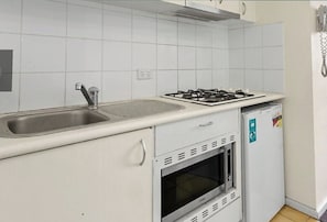 Compact kitchen area with an oven, stainless steel sink, and small refrigerator.