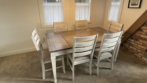 Una sala menjador amb taula de fusta i sis cadires, un lampadari i finestres amb cortines.