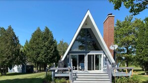 A modern A-frame house with a glass front and a brick chimney. - Four-season lakefront charm in Northern Michigan (Harbor Springs)