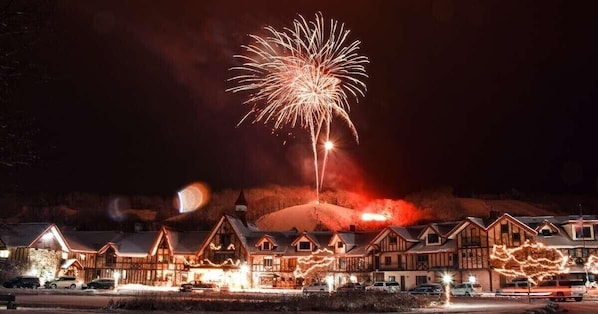 Un hotel con varias construcciones, una montaña nevada al fondo y un espectáculo de fuegos artificiales.